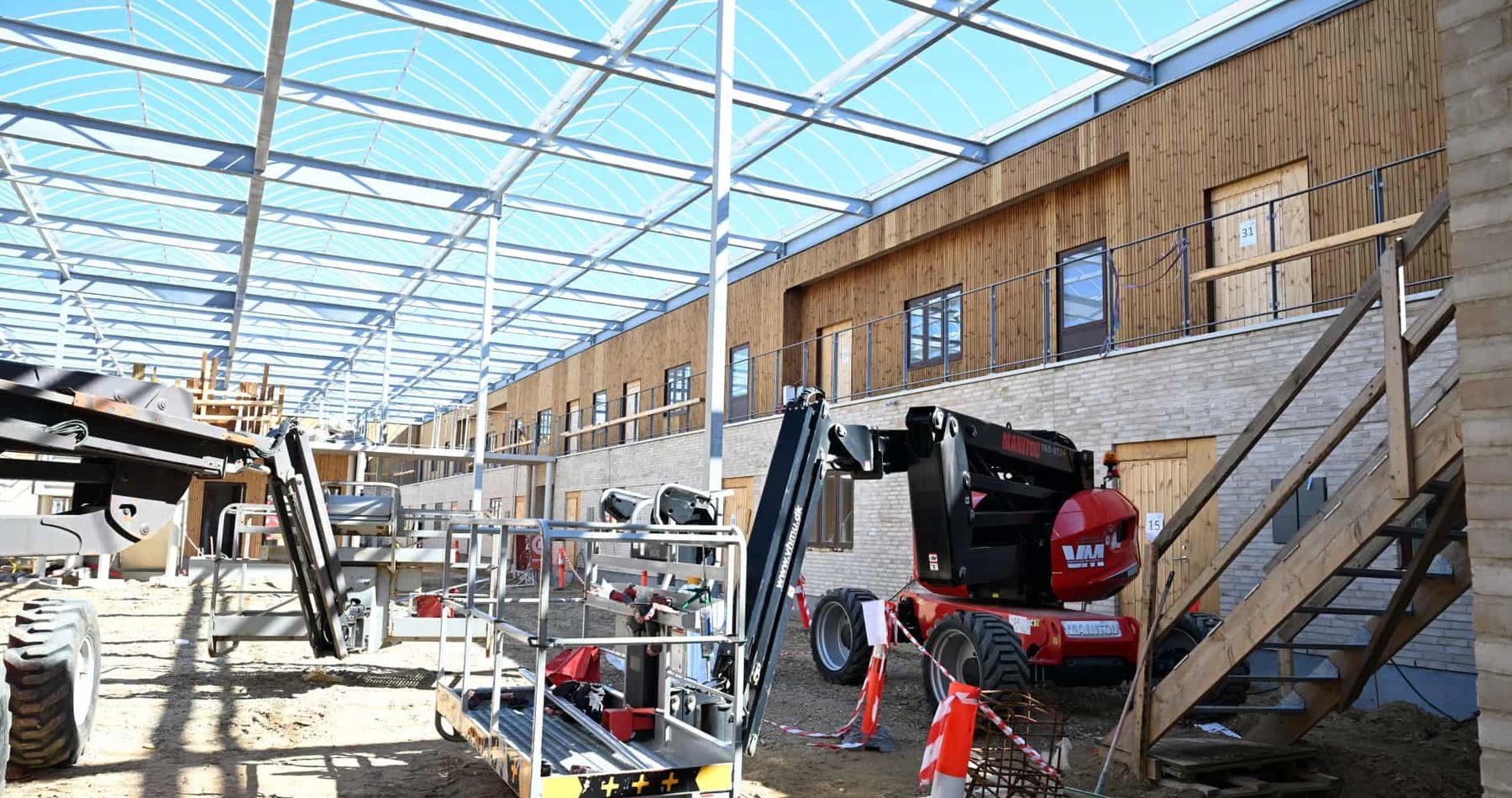 Foto: atriumgården under opførelse med stålkonstruktion, lifte og træbeklædte svalegange