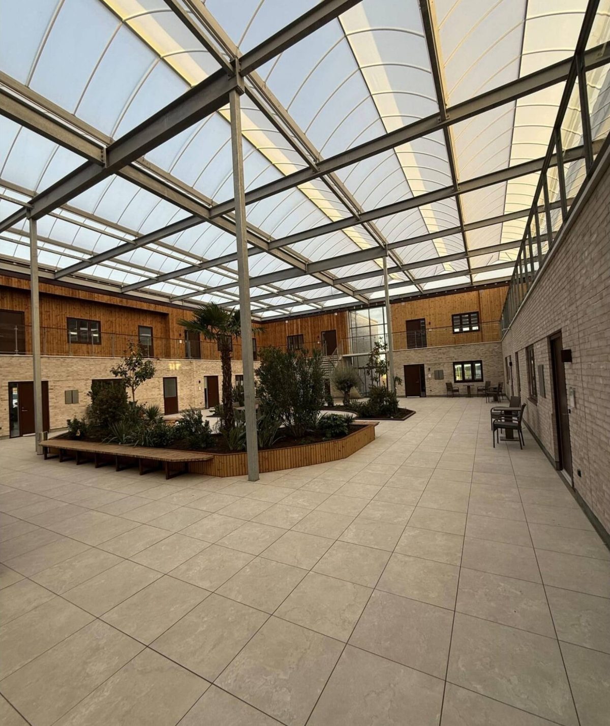 Foto: atriumgården i stueplan med palme, plantebed med træbænk og caféborde langs facaden