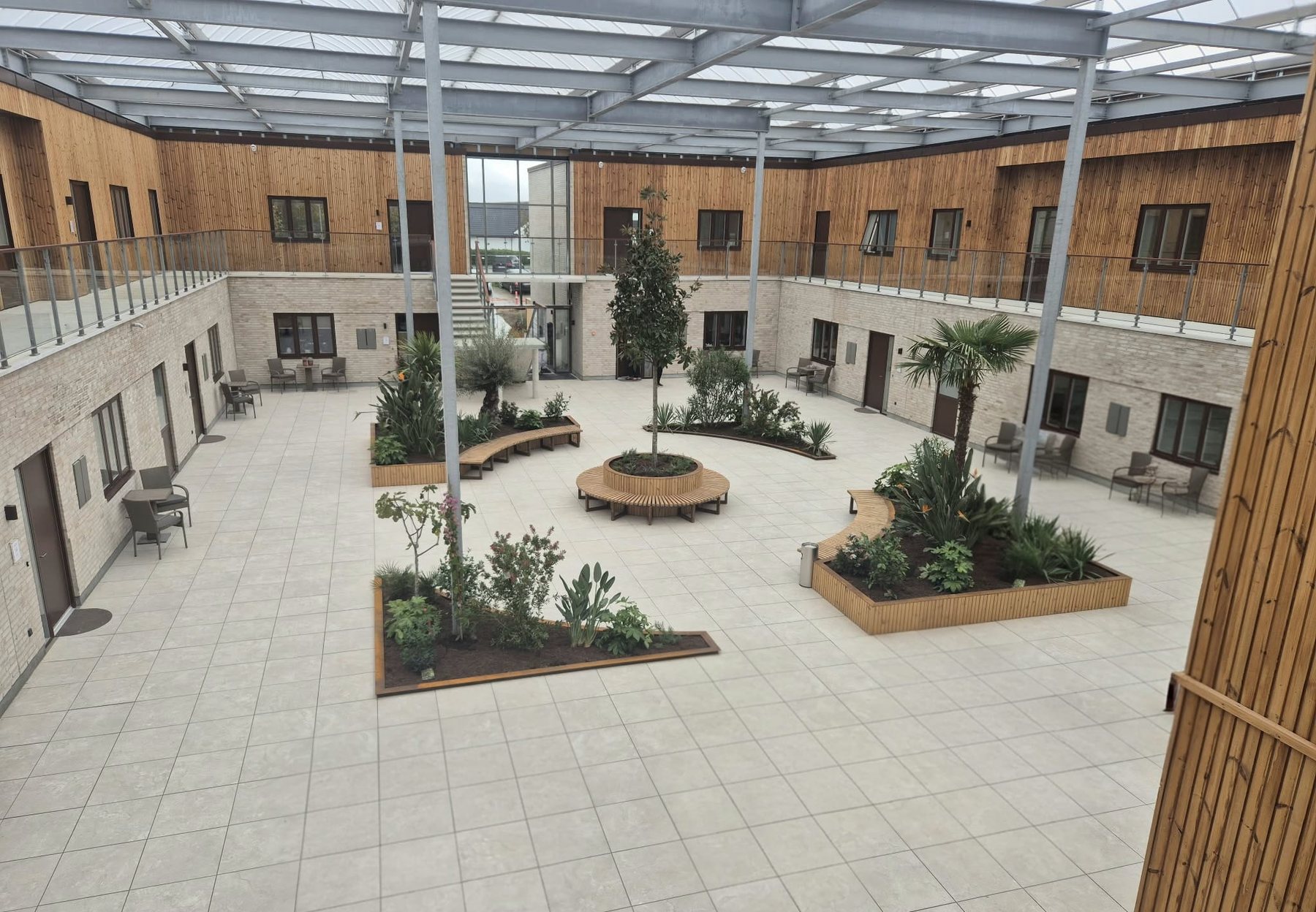 Foto: atriumgården med lys tegl i stueetagen, lodret træbeklædning på første sal og plantebede i træ og stål